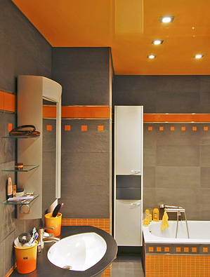 Ansicht eines grau-orangen Badezimmers mit orangefarbener Hochglanzdecke mit integrierter Beleuchtung in Form quadratischer Spots